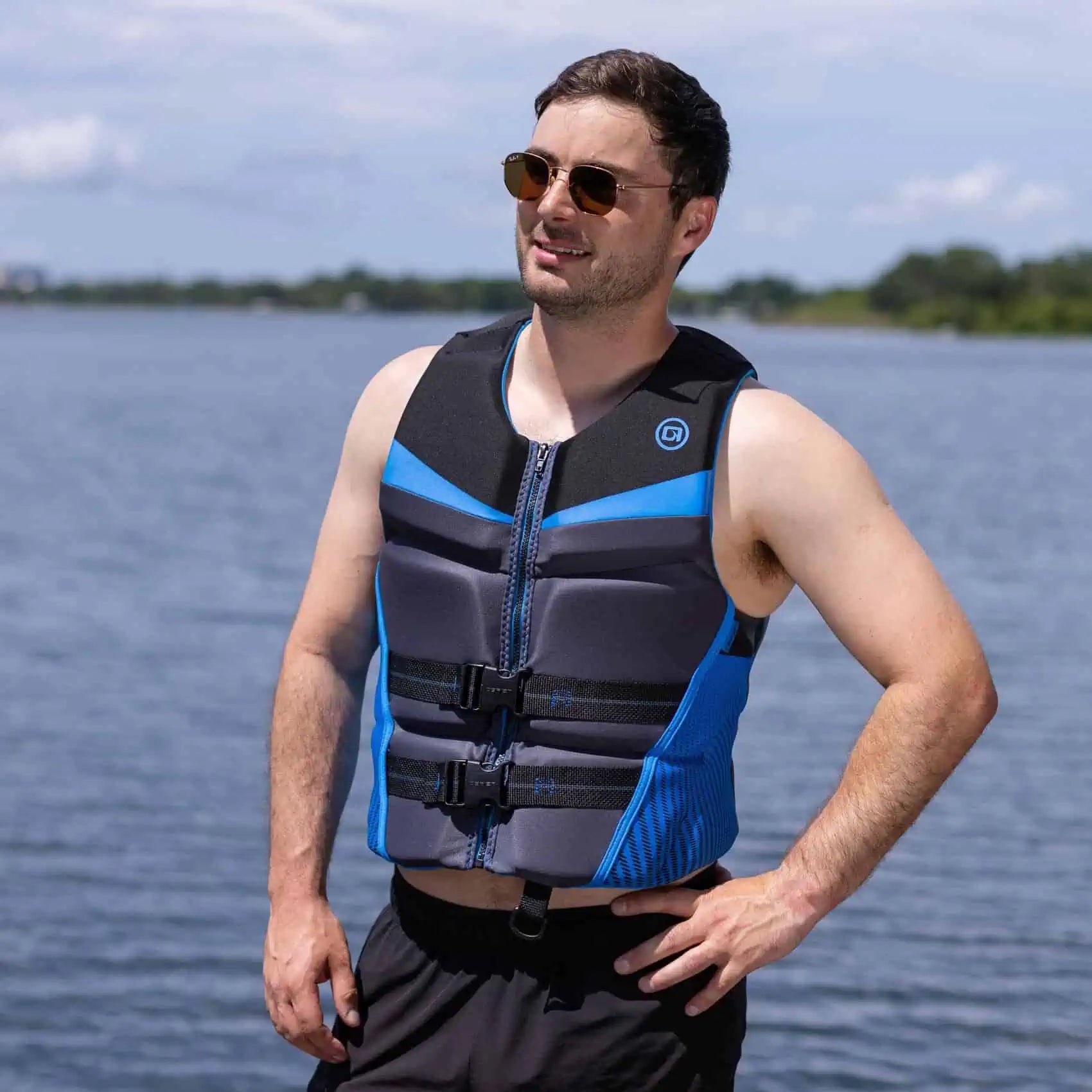 Man wearing a blue and black O'Brien Men's Flex V-Back Life Jacket by a body of water
