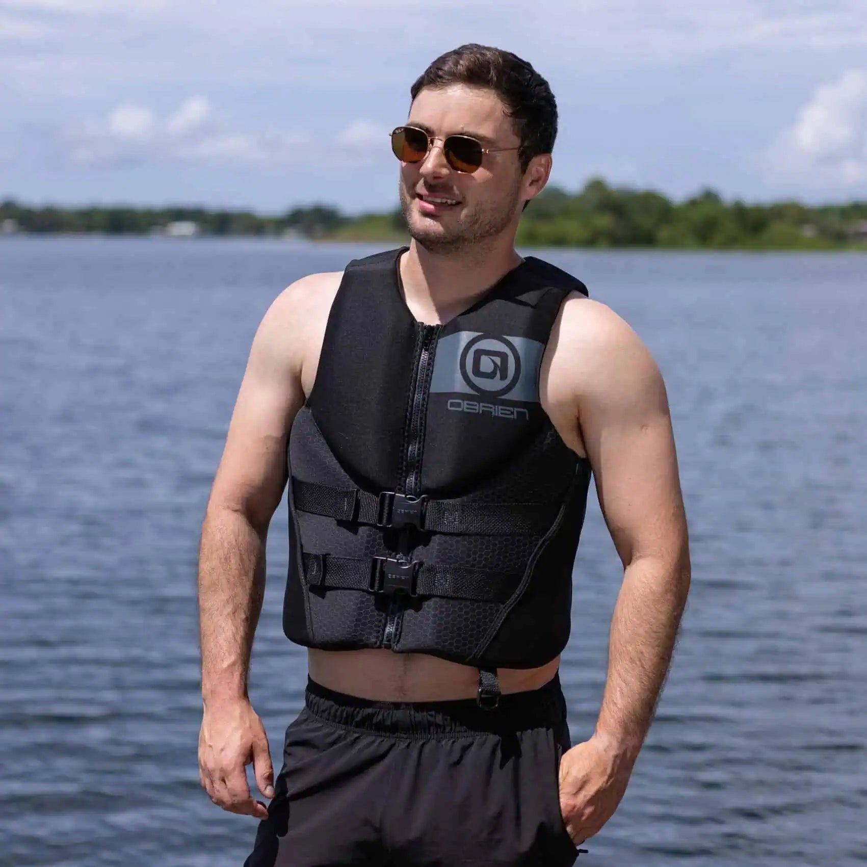 Man wearing a black O'Brien Men's Traditional Vest with a brand logo by a body of water.