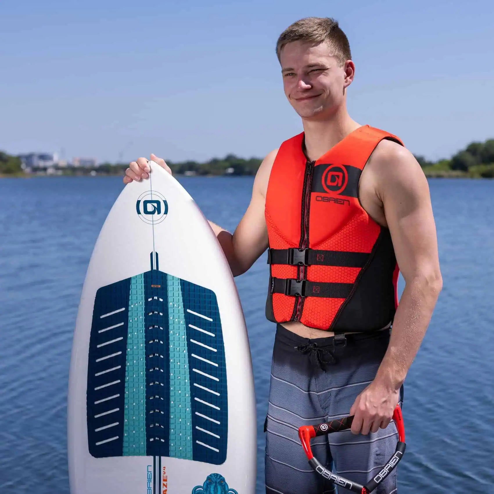 Man holding a surfboard with a lake and clear sky in the background O'Brien Men's Traditional Vest