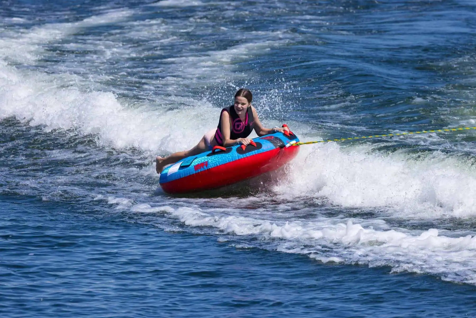 Person riding a red and blue inflatable O'Brien Screamer Tube on waves in the water