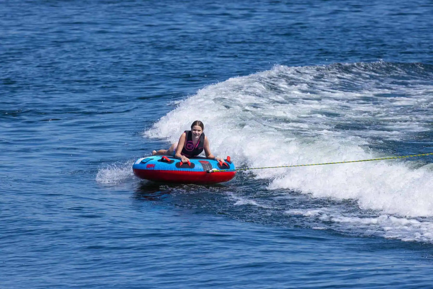 Person on a red and blue O'Brien Screamer Tube being pulled by a rope in the water.