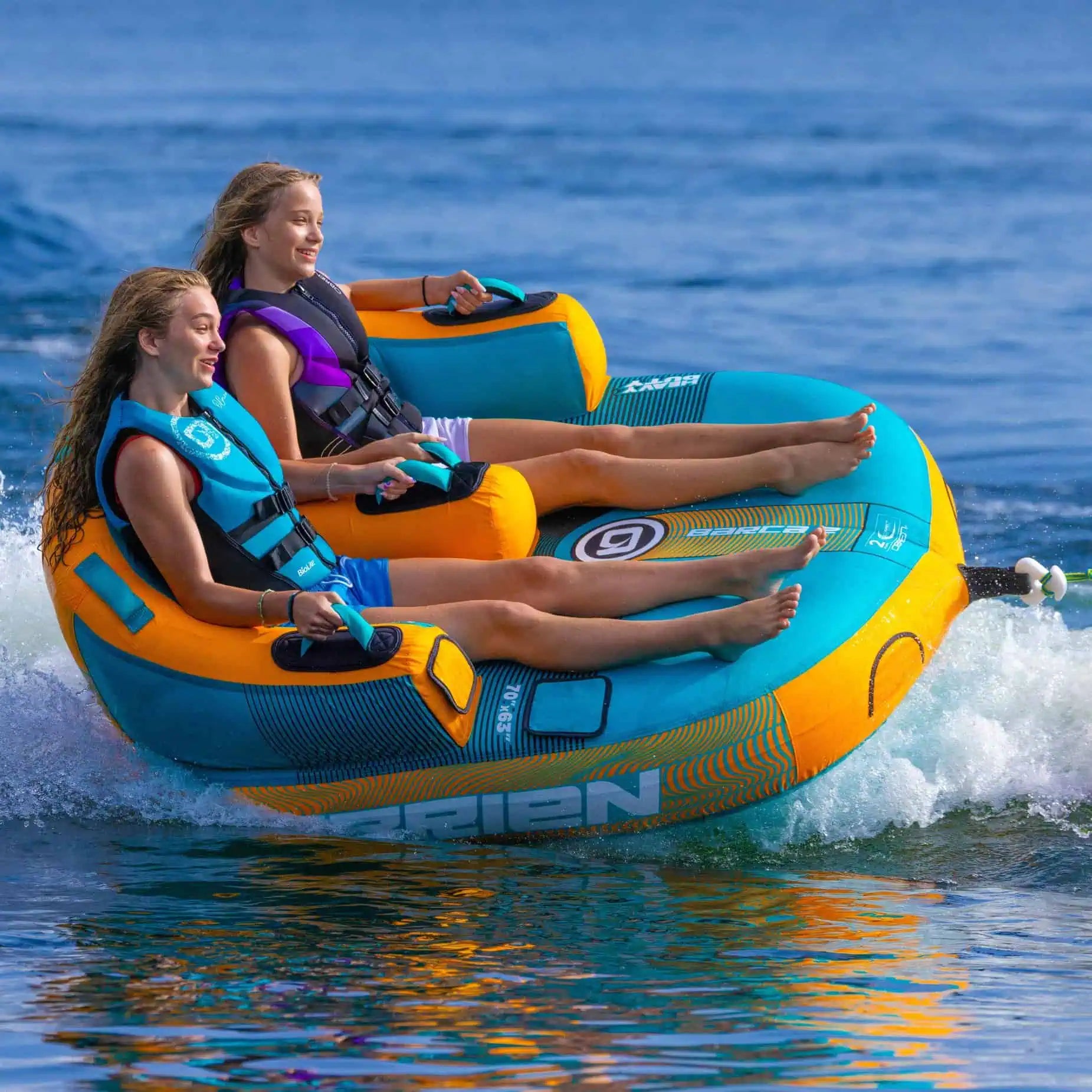 Two people on a blue and orange O'Brien Barca - 2 Person Towable Boat Tube in the water.