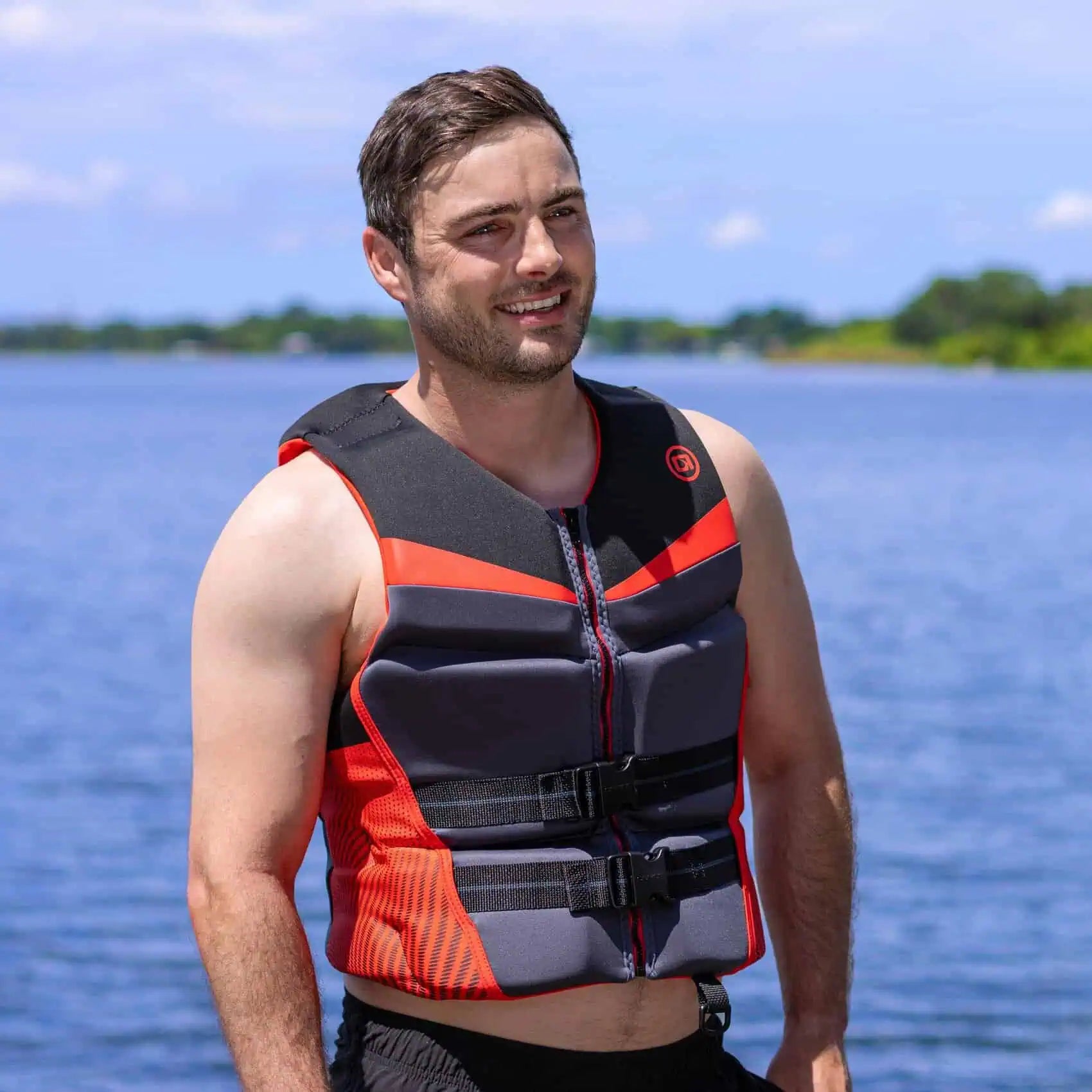 Man wearing a red O'Brien Men's Flex V-Back Life Jacket standing by a body of water.