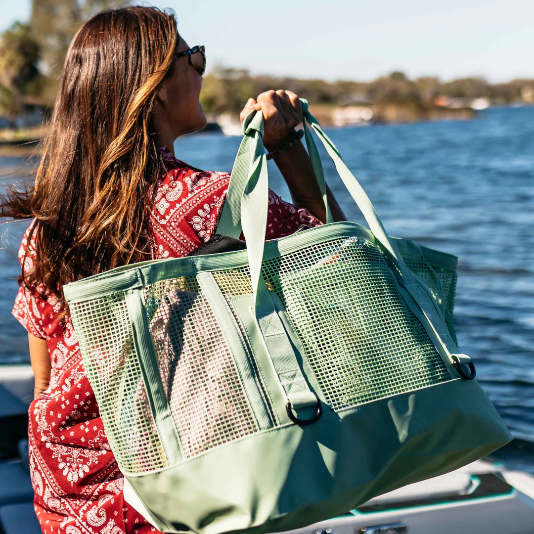 Woman holding the sage Mission Cassi Gear Tote - Heavy-Duty Boat and Beach Bag by a body of water