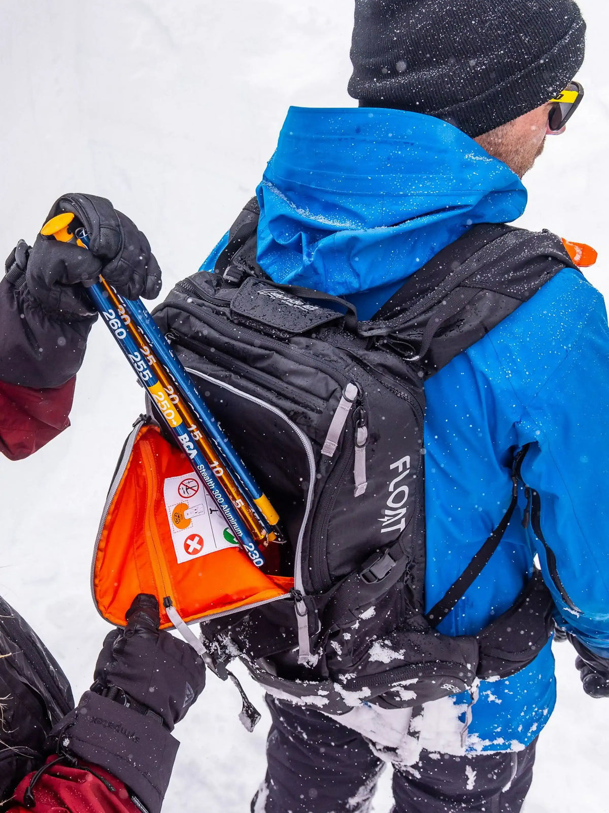 one person is putting an avalanche probe into the BCA Float E2-25 Turbo Avalanche Airbag worn by another person