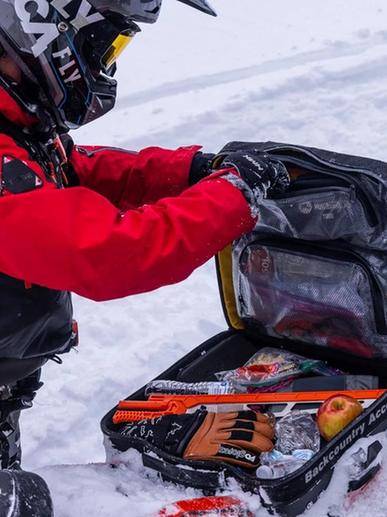 Person in winter gear opening a BCA Mtn Pro Tunnel Bag in the snow.
