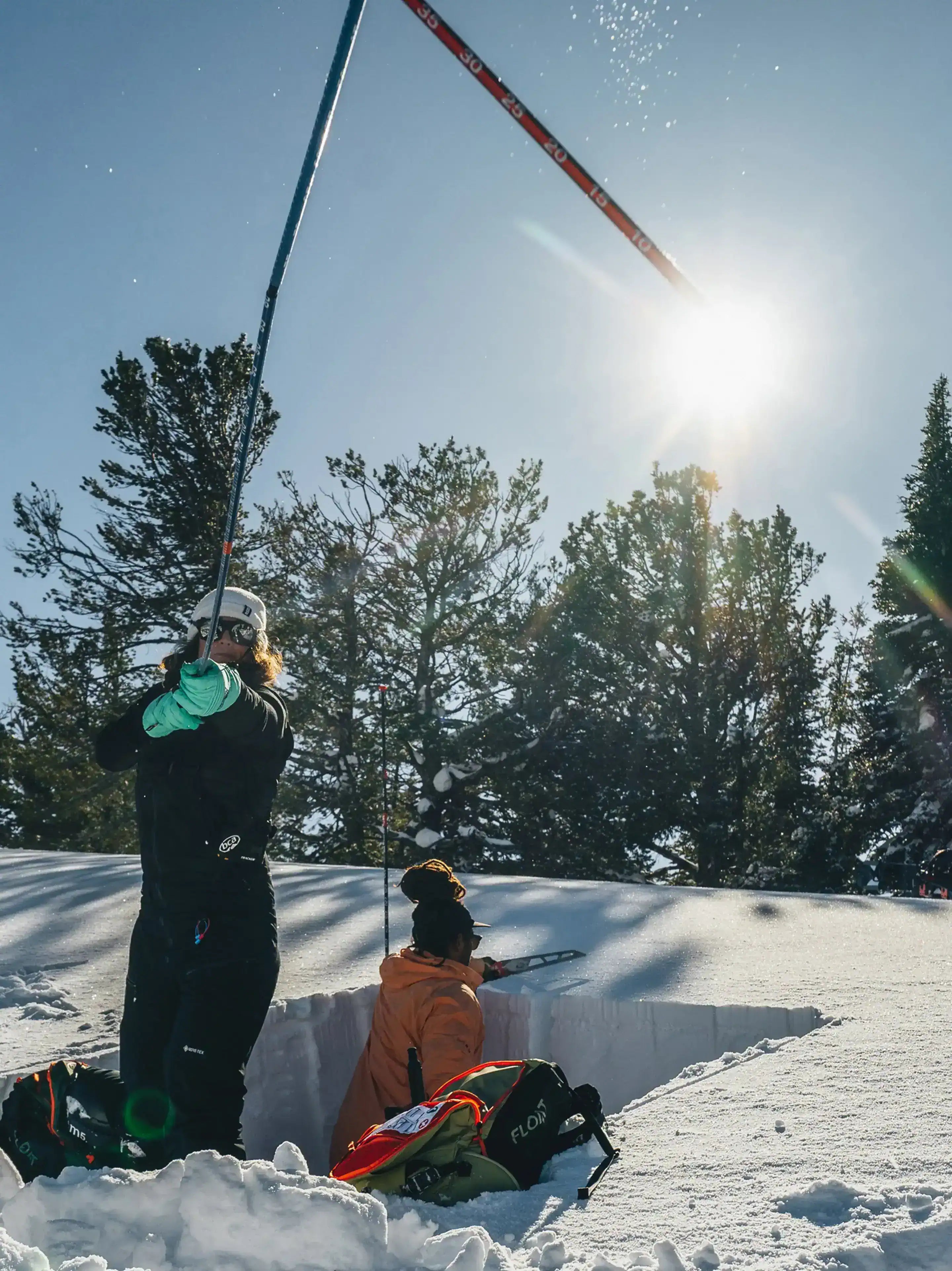 Two people in winter gear on a snowy slope deploying the BCA Stealth 330 Avalanche Probe