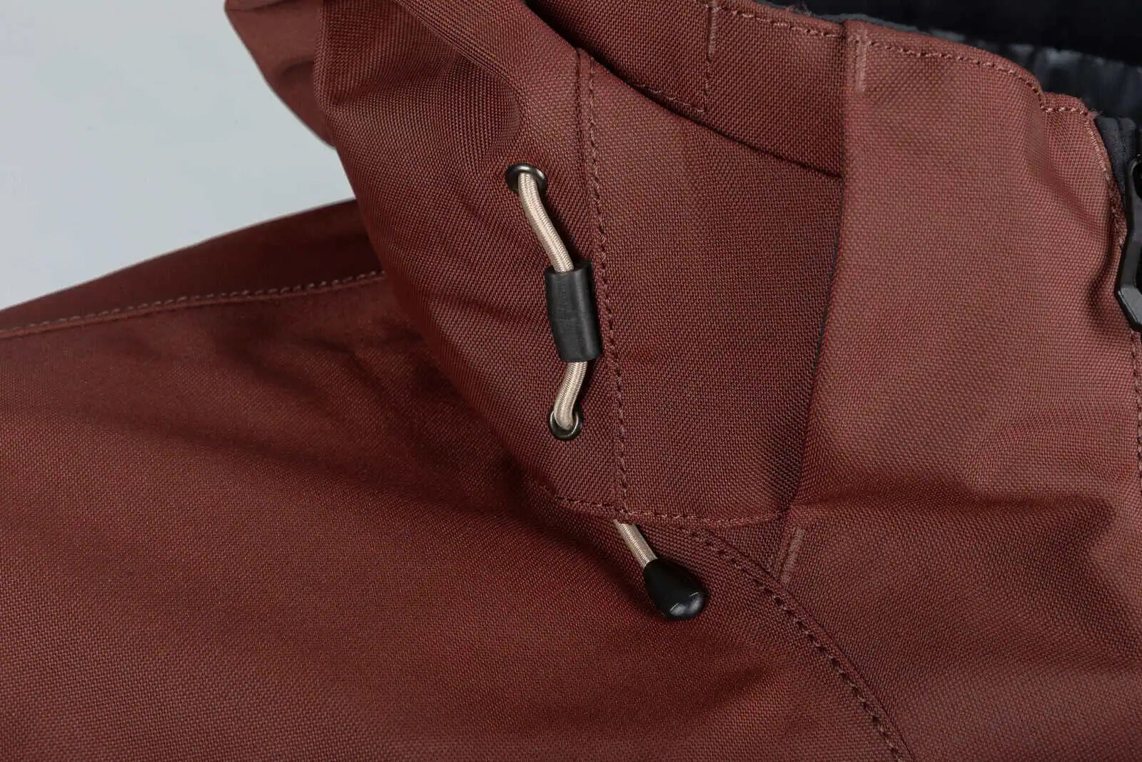 Close-up of a Klim Lochsa One-Piece Monosuit - Bitter Chocolate - Montana Tan showing the collar, drawstring toggle, and zipper area against a light neutral background.