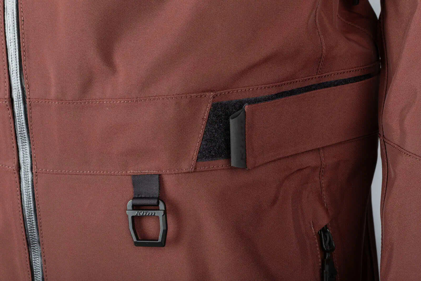 Close-up of a Klim Lochsa One-Piece Monosuit - Bitter Chocolate - Montana Tan with a front zipper, a flap pocket, and a black D-rig loop closure.