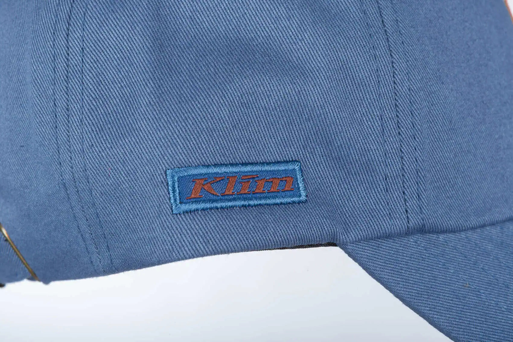 Close-up of a blue Klim Peak Hat with a rectangular embroidered Klim logo patch on the side.