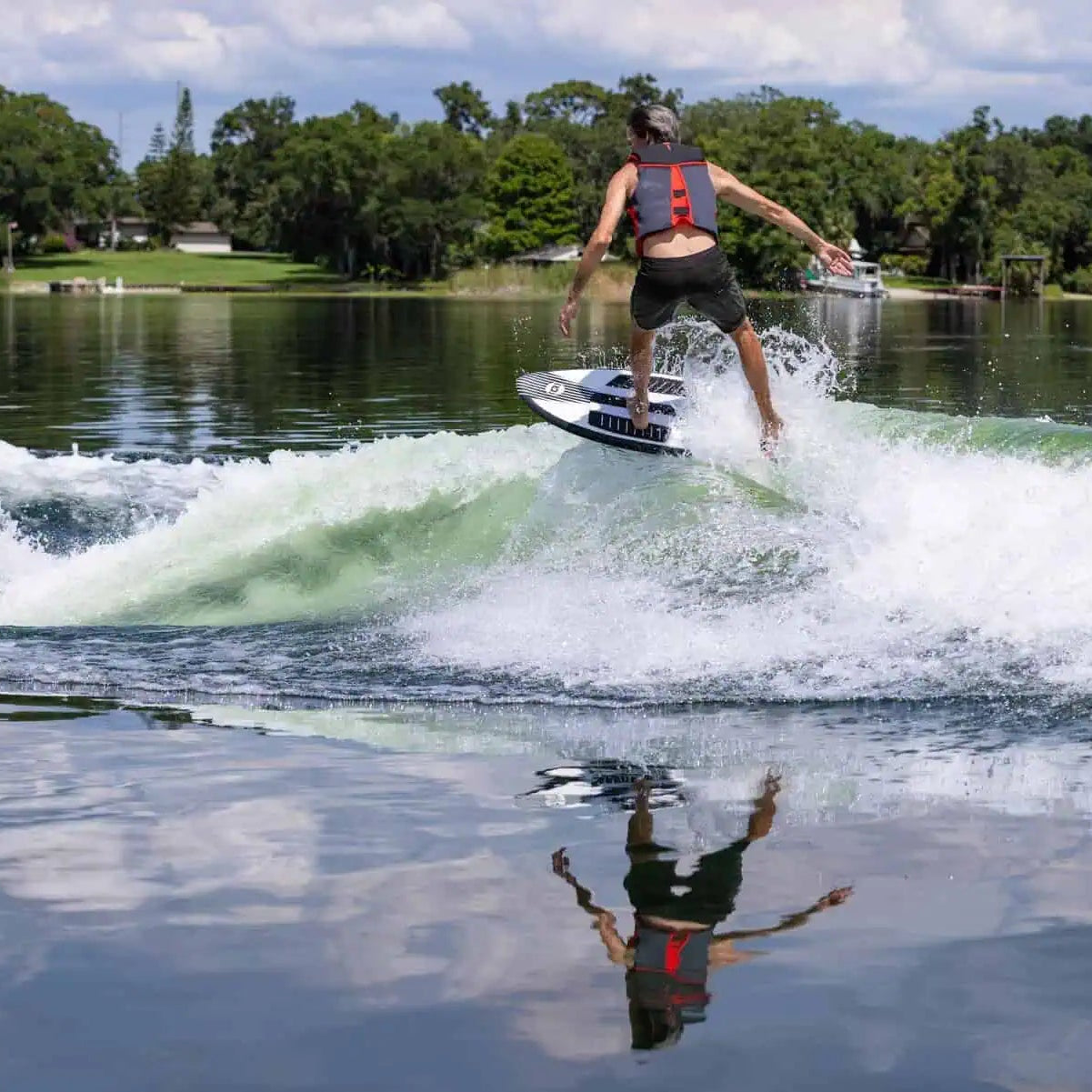 Person wakesurfing on a lake with trees and a houseboat in the background