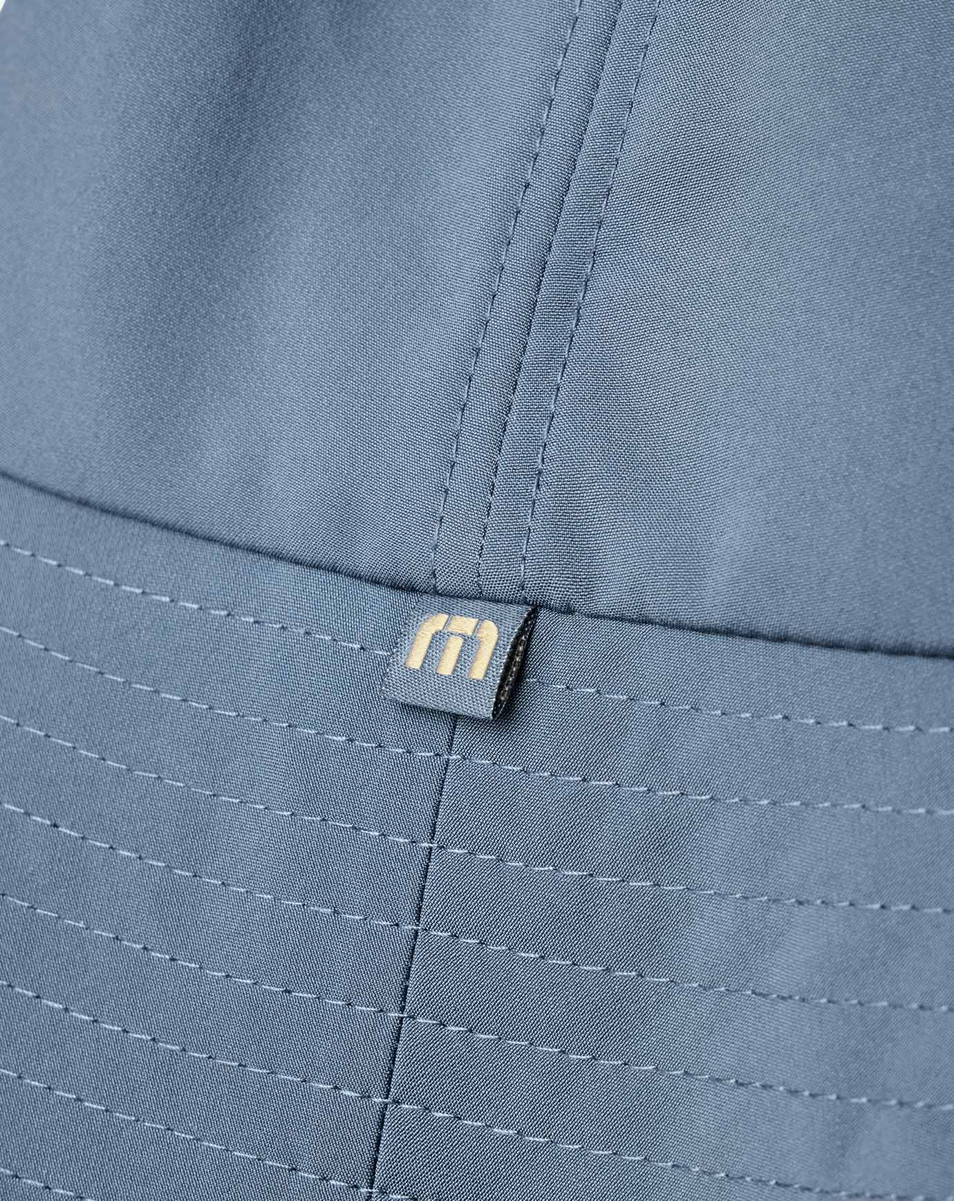 Close-up of a blue fabric with a brand logo on country club bucket hat from Travismathew