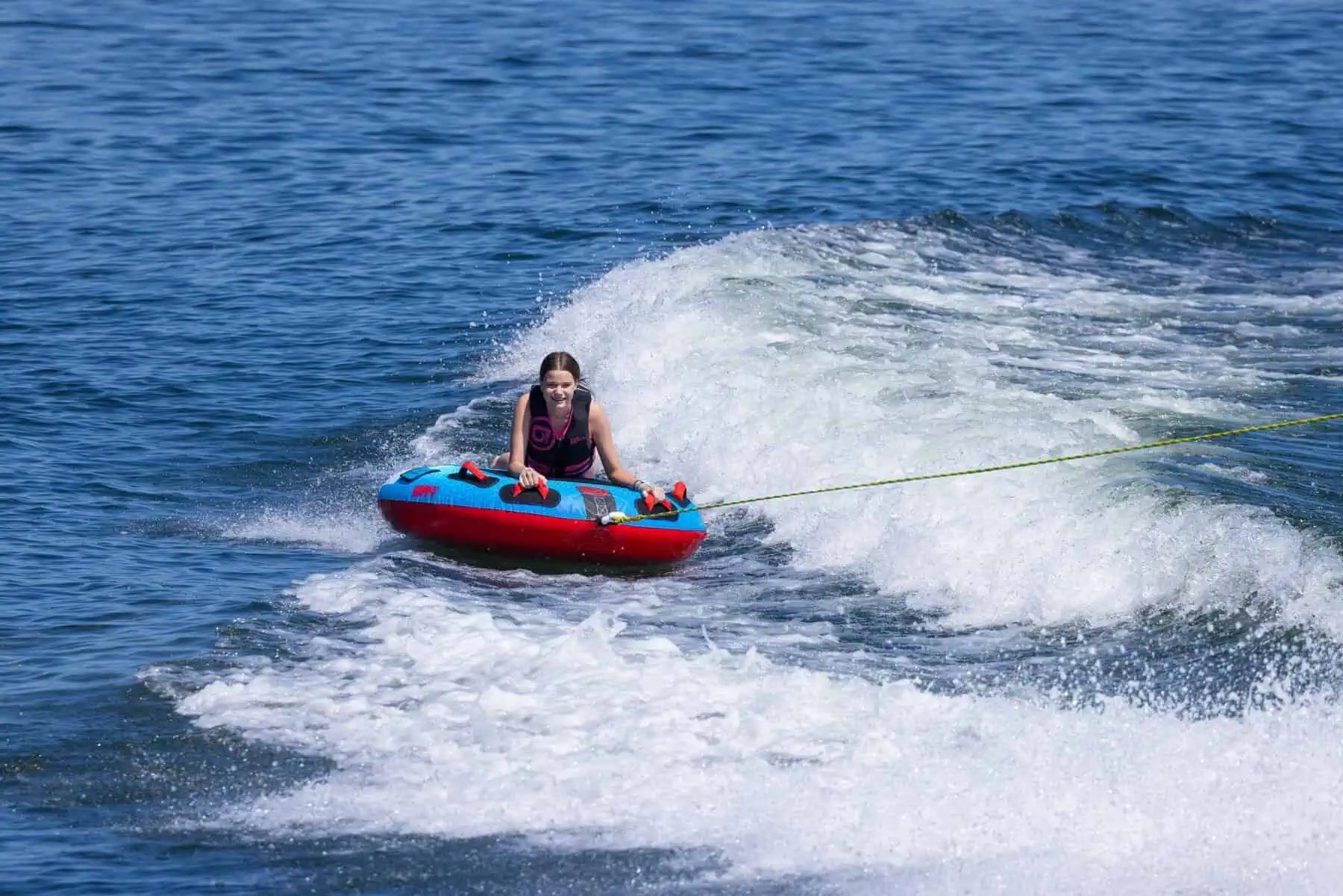 Person on a red and blue O'Brien Screamer Tube being pulled by a rope in the water.