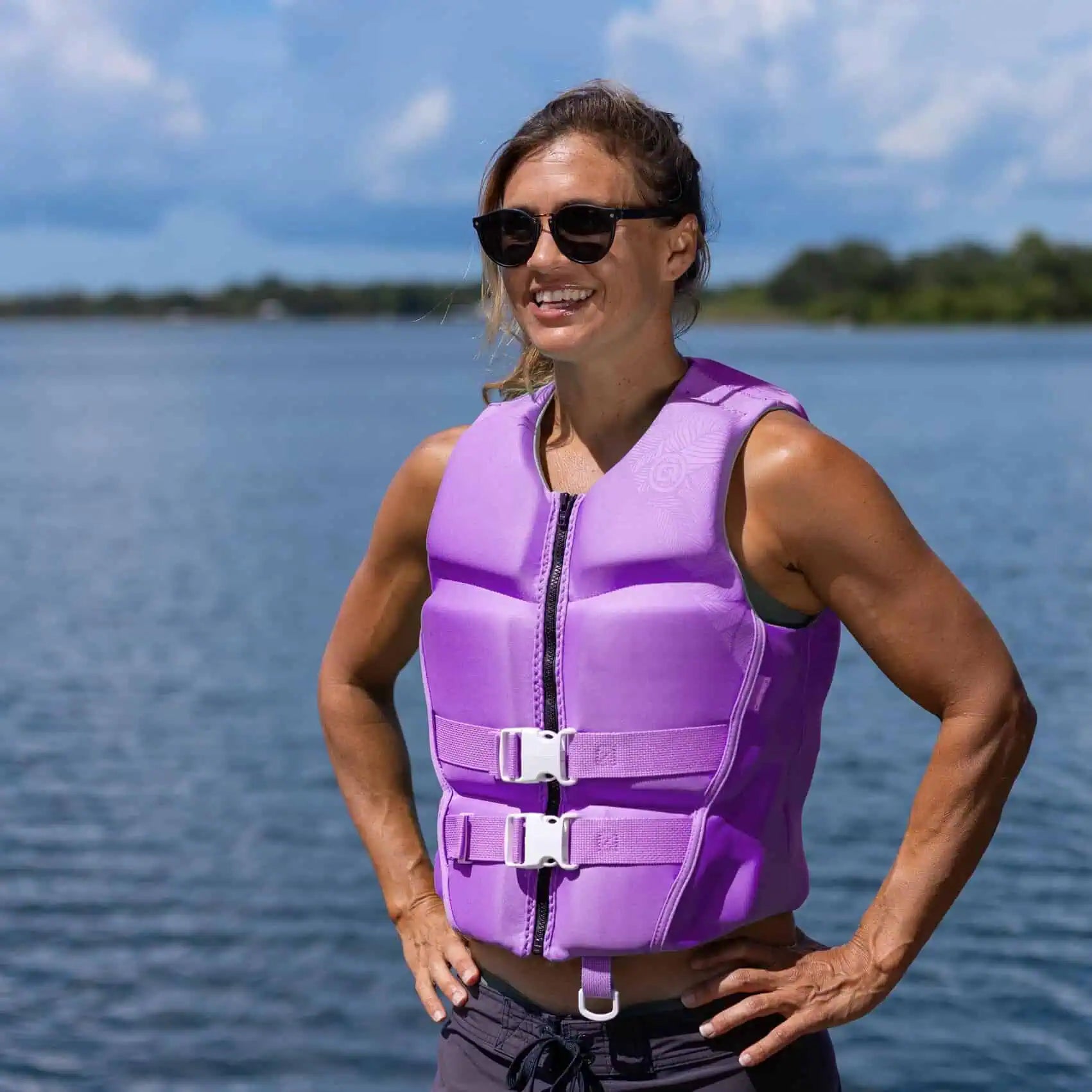 Woman wearing a lavender O'Brien Ladies Flex V-Back Life Jacket standing by a body of water.
