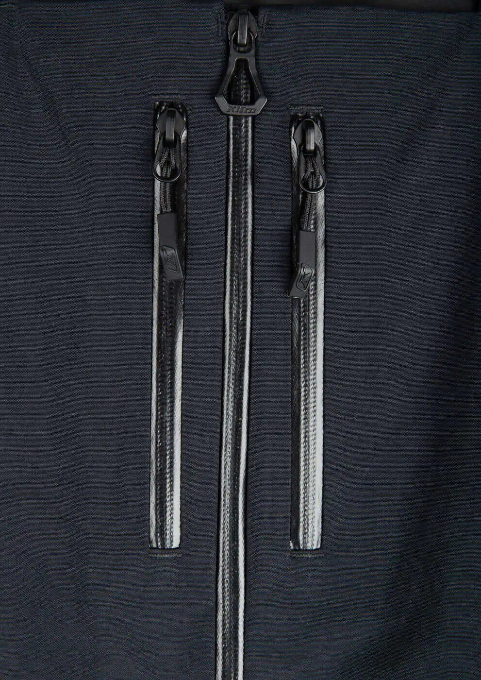 Close-up of a Klim Togwotee Bib featuring a central vertical zipper and two parallel horizontal zippered pockets with black zippers.