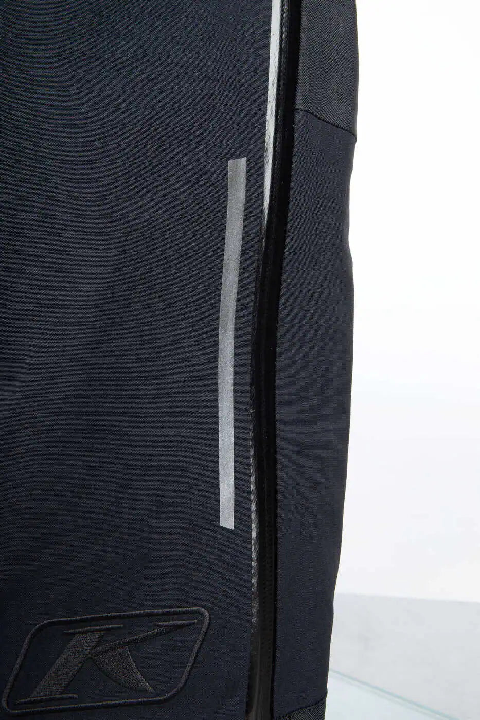 Close-up of a Klim Togwotee Bib showing a vertical reflective strip and a black embroidered stylized 'K' logo near the bottom.