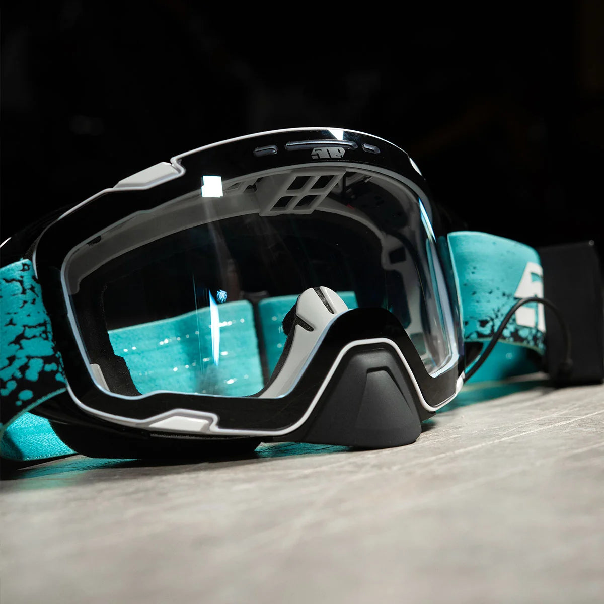 the 509 Aviator 2.0 Ignite S1 Heated Snowmobile Goggle - Glacier Blue is lying on a  grey surface with black background