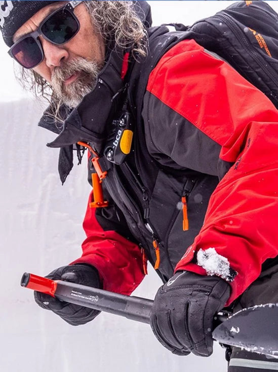 Person in red and black winter clothing with a BCA BC Link Two-Way Radio 2.0, holding an ice axe on a snowy background