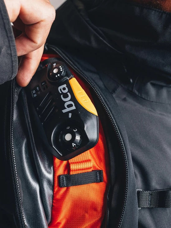 Close-up of a person opening a black backpack with a BCA BC Link Two-Way Radio 2.0 inside.