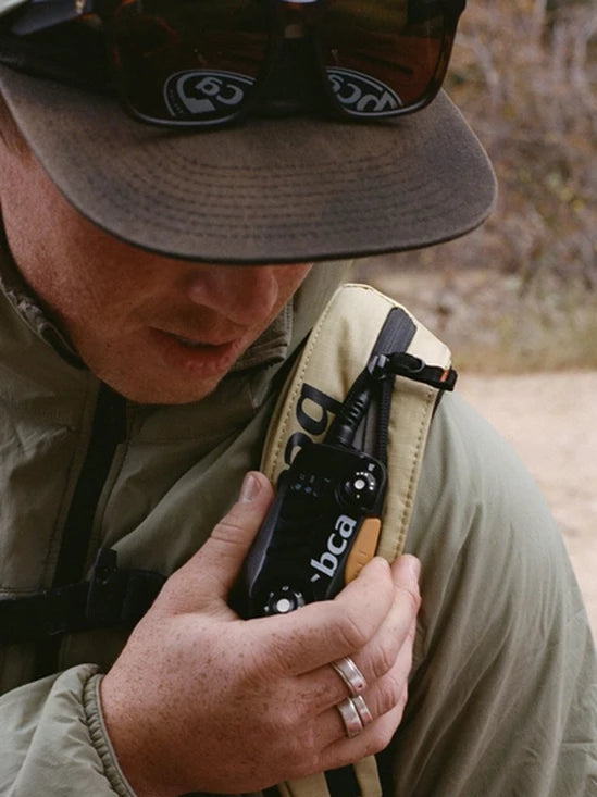 Person holding a backpack with a BCA BC Link Two-Way Radio 2.0 outdoors
