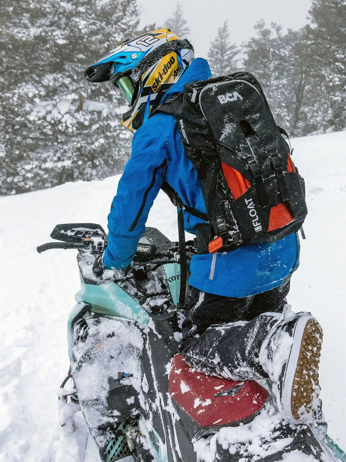 a person is riding a snowmobile and wearing the black BCA Float E2-25 Turbo Avalanche Airbag