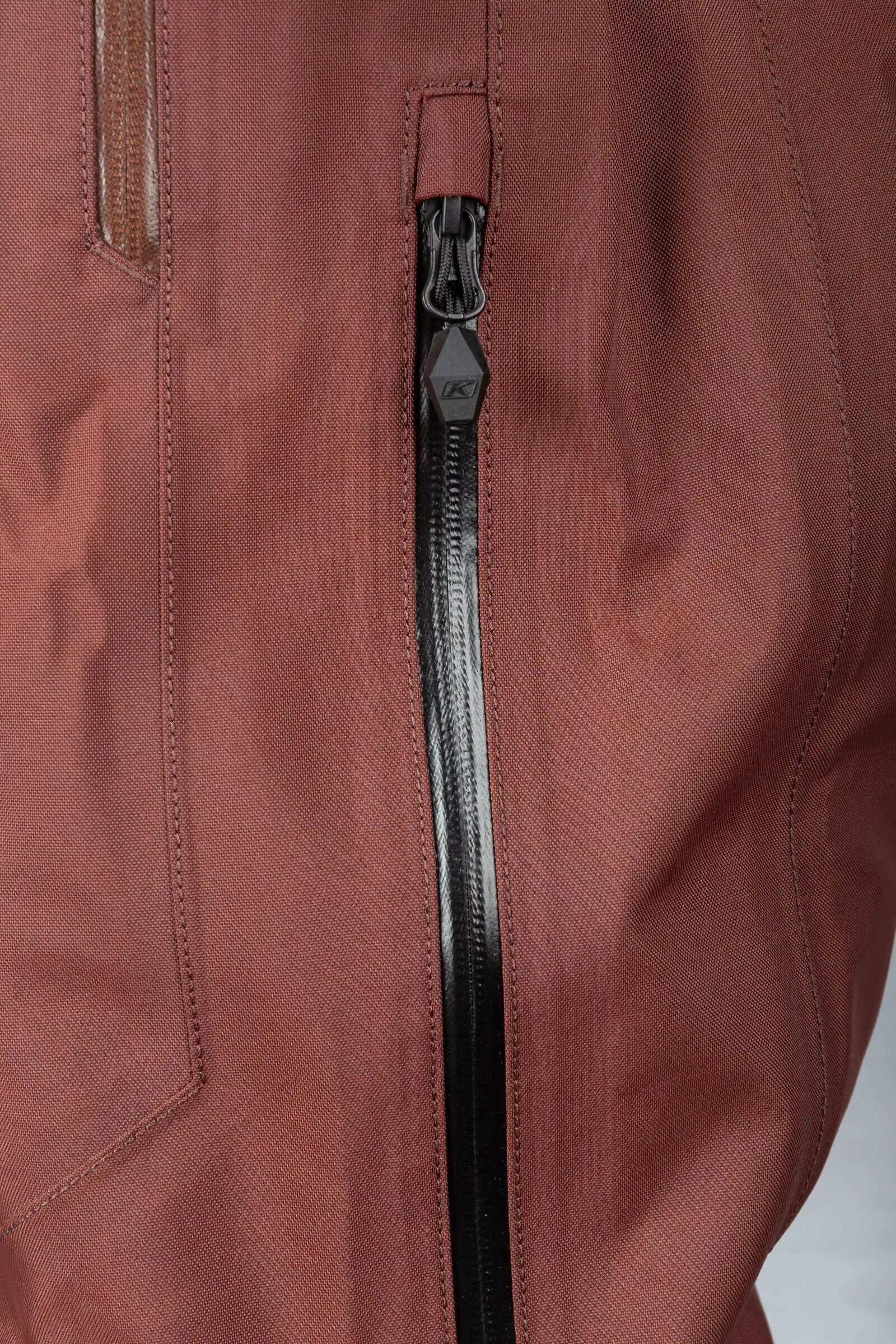 Close-up of a Klim Lochsa One-Piece Monosuit - Bitter Chocolate - Montana Tan with a prominent black zipper running vertically down the center.