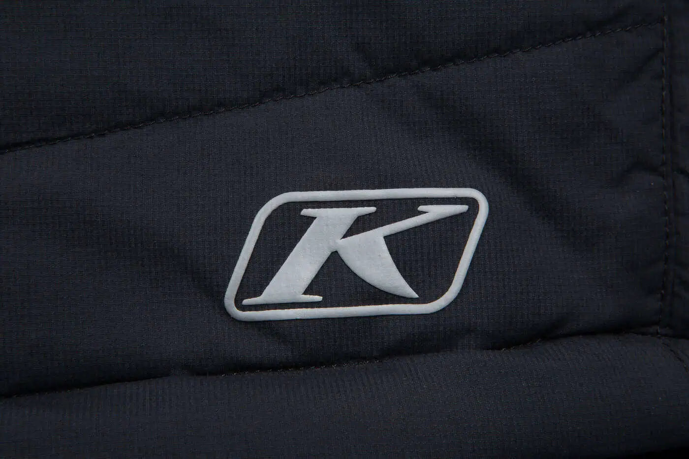 Close-up of a black Klim Men's Override Vestwith a white logo on a dark background