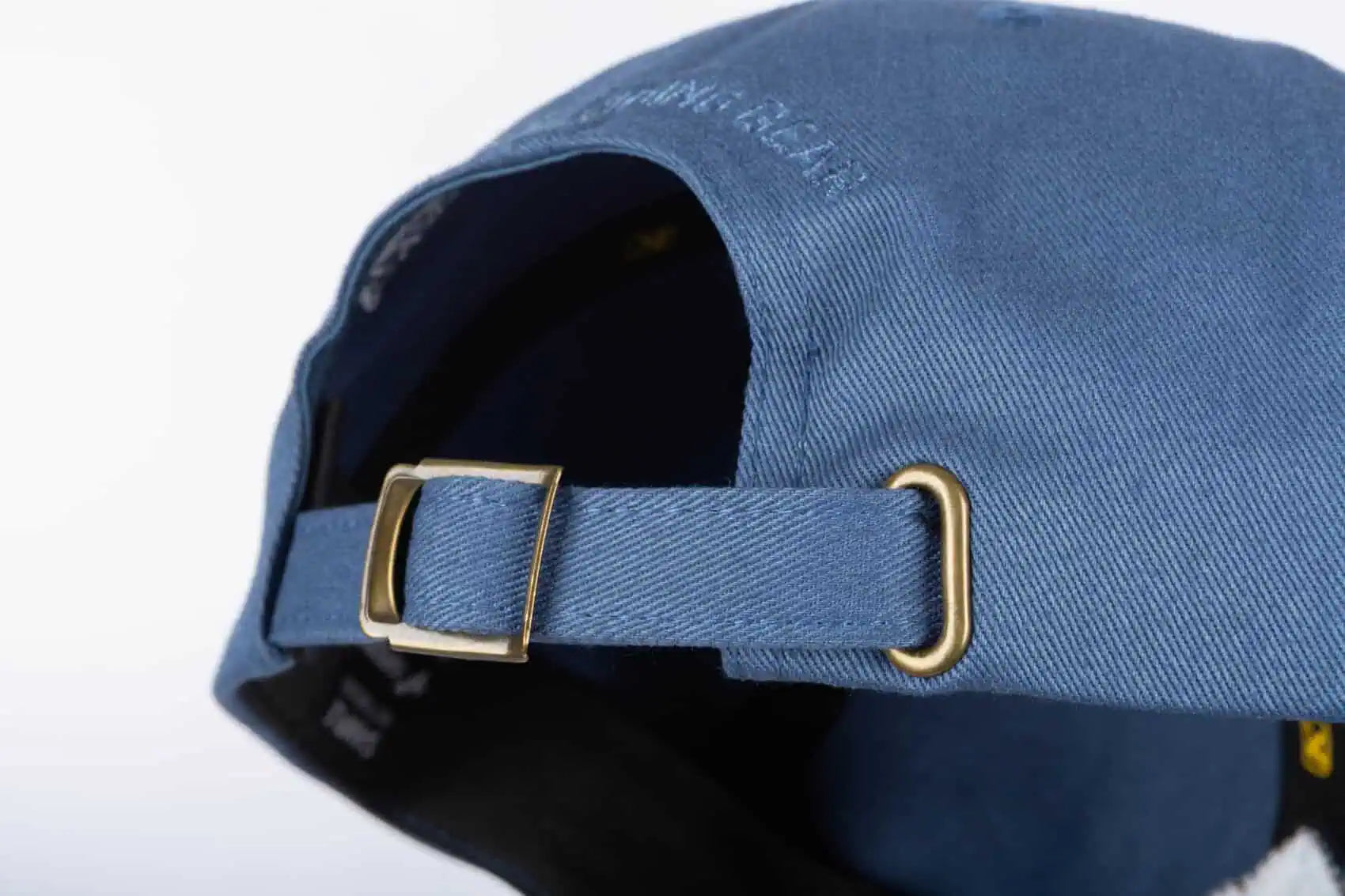 Close-up of the back of a blue Klim Peak Hat with an adjustable fabric strap and gold-tone metal buckle.