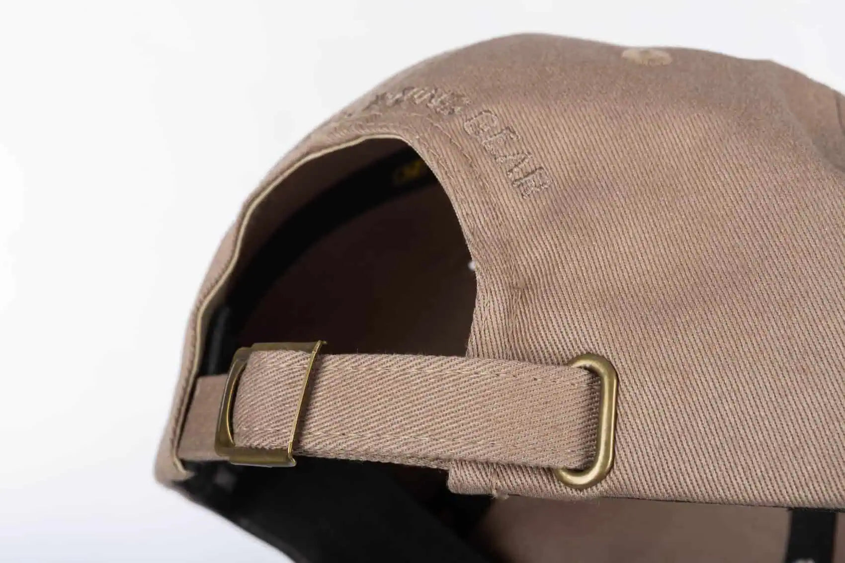 Close-up of the back of a walnut colored  Klim Peak Hat with a matching fabric strap and brass buckle, on a white background.