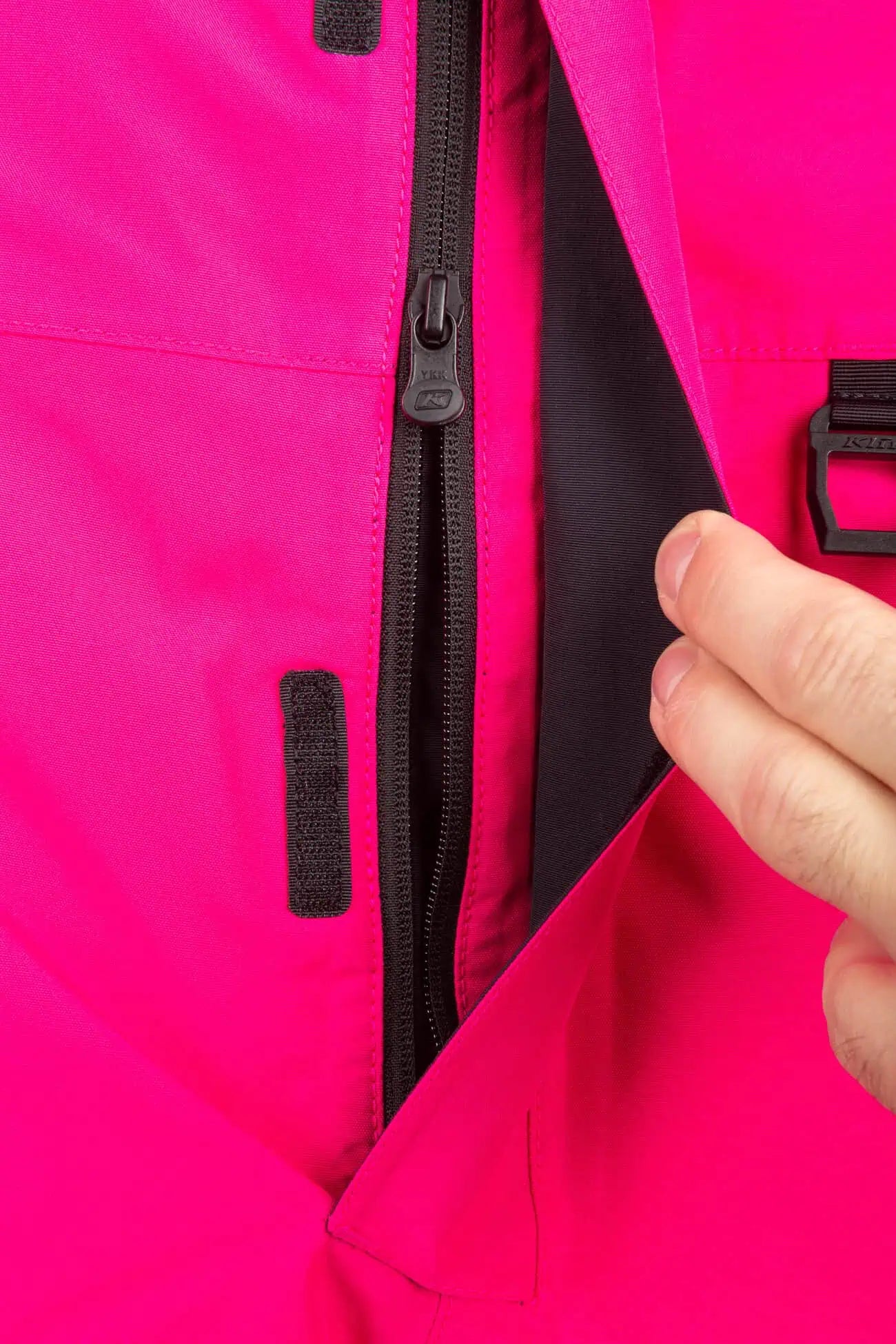 Close-up of a hand opening a black zipper on a bright pink Klim Terrain One-Piece Monosuit.