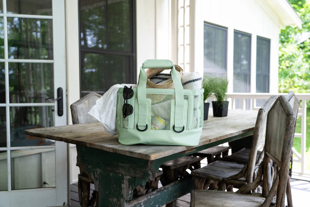 Light sage Mission Cassi Gear Tote - Heavy-Duty Boat and Beach Bag on a wooden table outdoors with a house in the background
