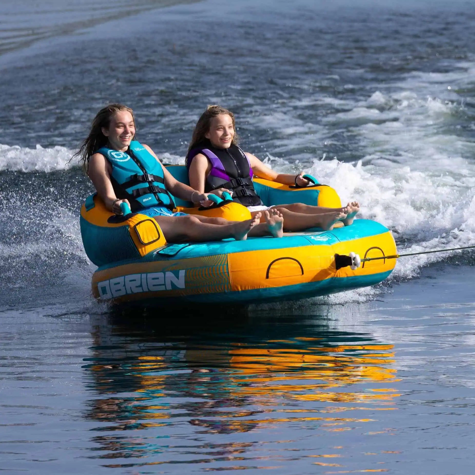 Two people on a blue and yellow O'Brien Barca - 2 Person Towable Boat Tube in the water.