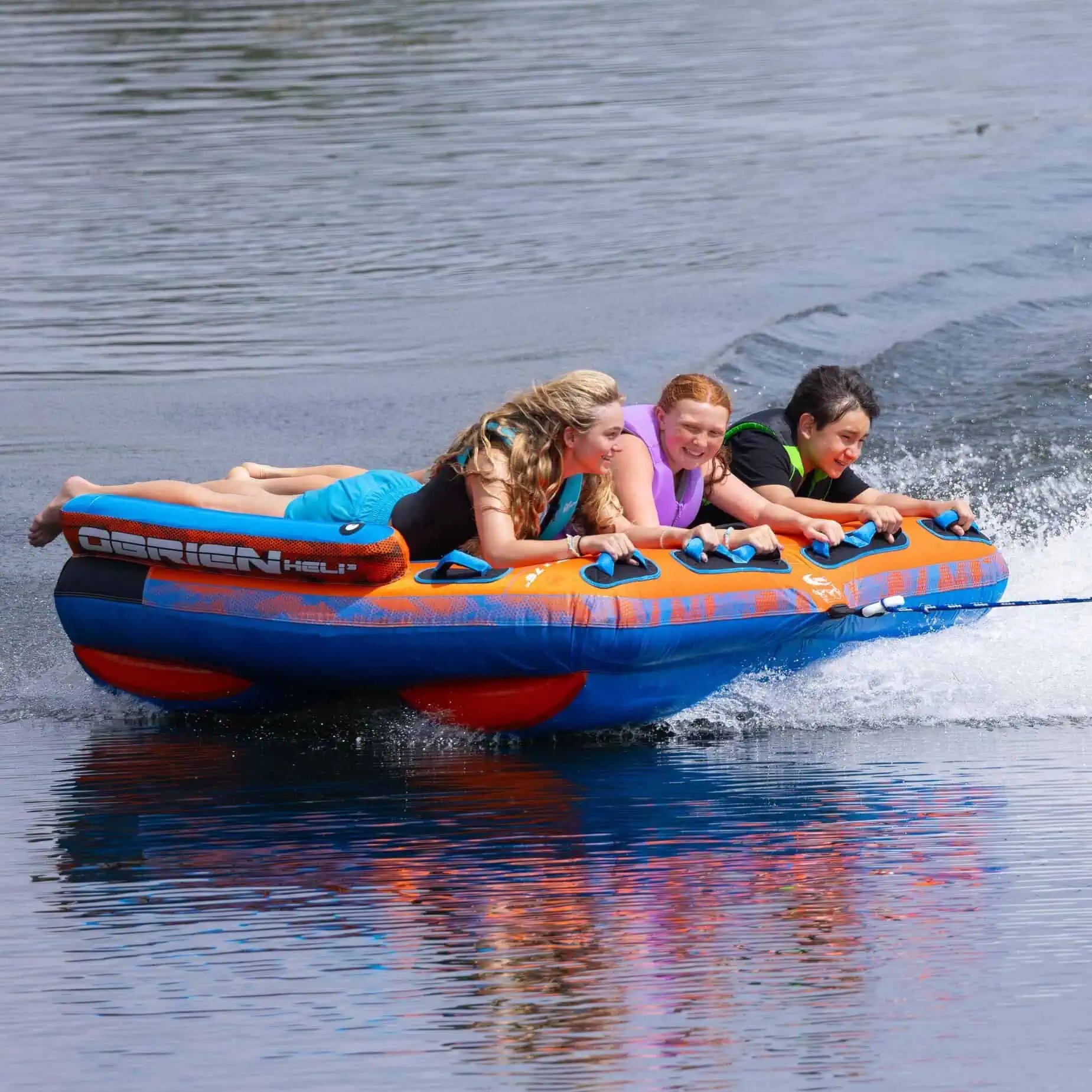 Four people on an inflatable O'Brien Heli 3 Boat Tube being pulled by a boat on water