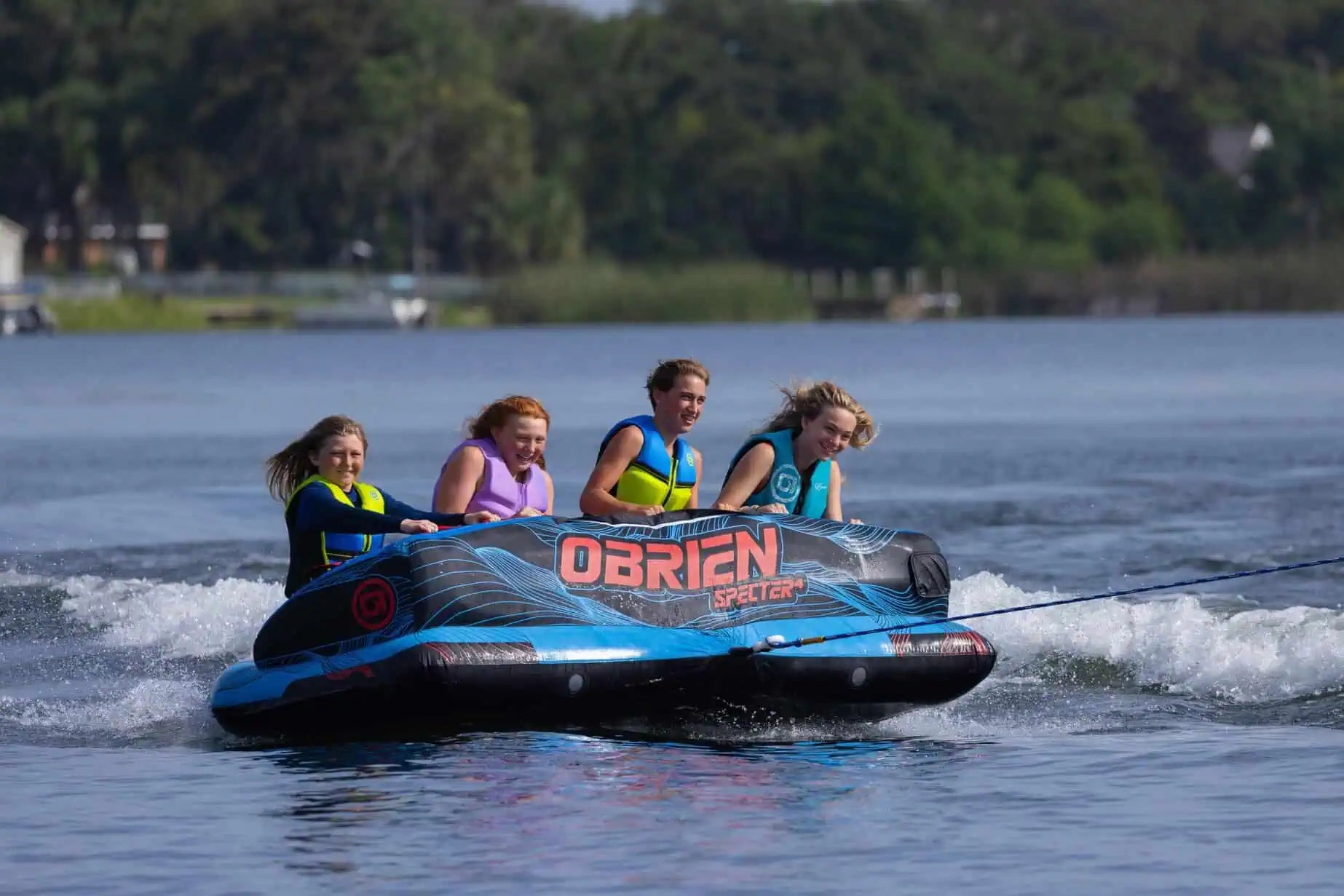 Four people on an O'Brien inflatable tube in a lake with trees in the background