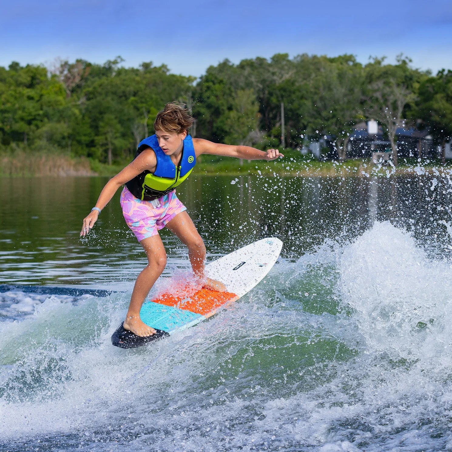Child wakesurfing on a lake with trees and a clear sky in the background with O'Brien Torrent Wakesurfer