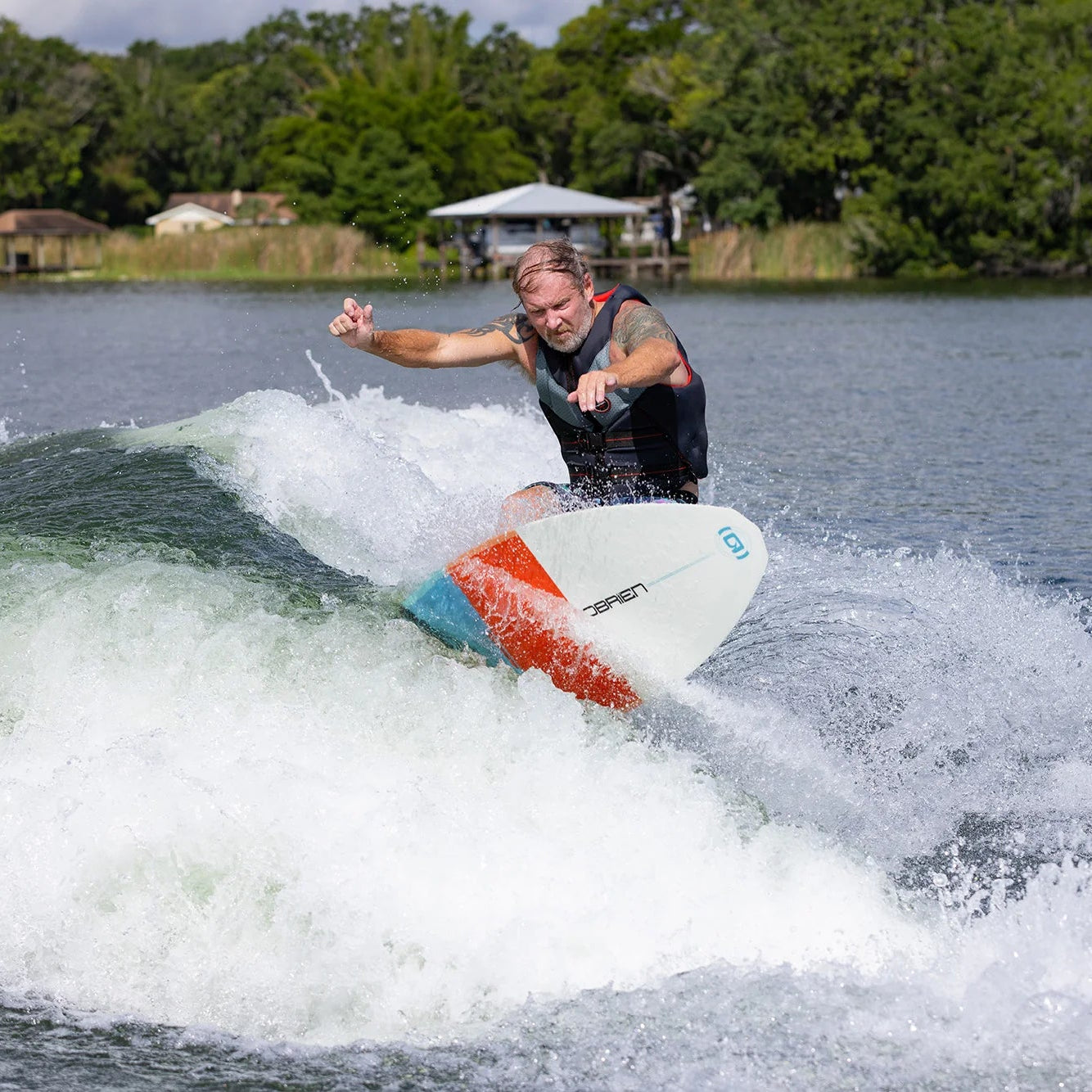 Person wakesurfing on a lake with trees and a dock in the background