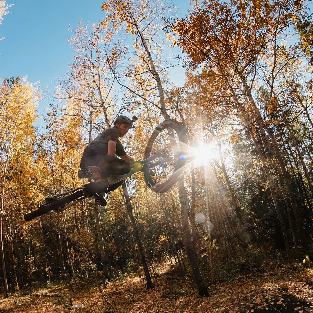 Person on a Vamoose Matador FS Downhill E-Bike in mid-air against a sunlit forest background