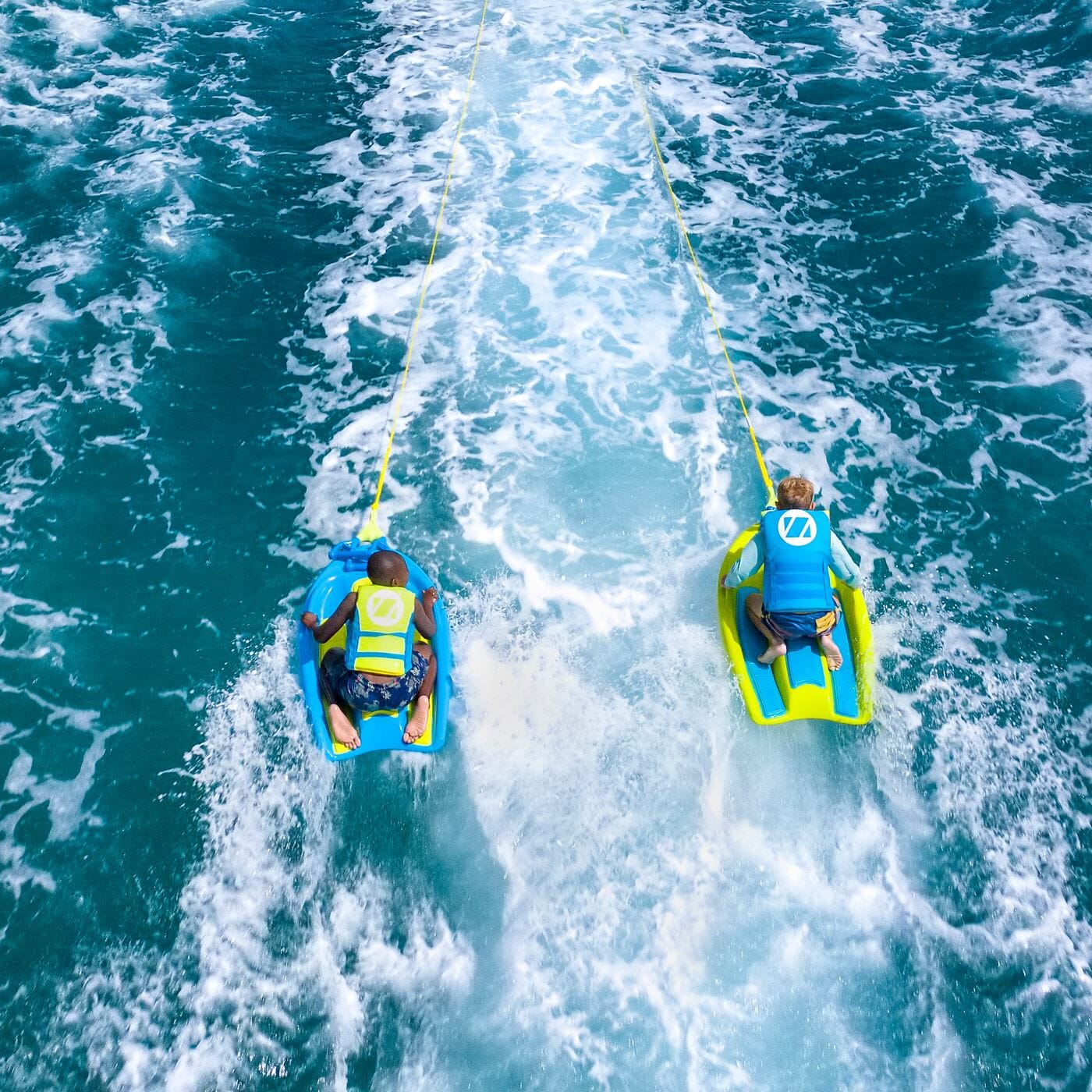Two people on ZUP Coast 80 Multi-Sport Board for Kids being pulled by a boat through blue water.
